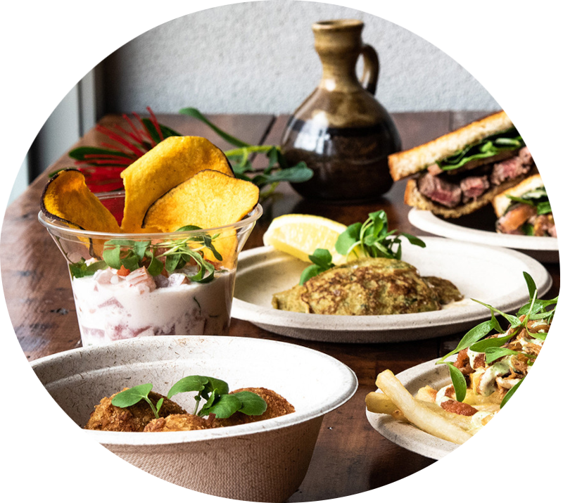 an array of salads, dips and sandwhiches with fresh garnish
            and a serving jug on a table